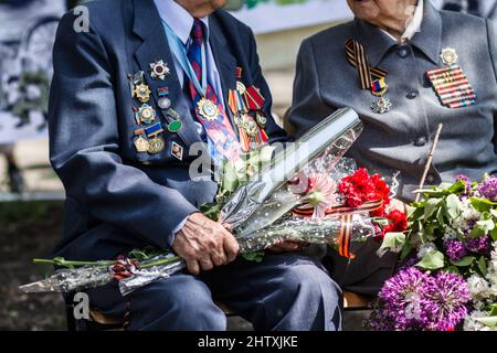 Einem lieben Freund Auf Wiedersehen sagen. Zugeschnittenes Bild von zwei Kriegsveteranen, die Blumen bei einem Begräbnis halten. Stockfoto