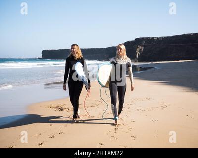 Surferinnen, die am Strand spazieren und auf die Wellen schauen Stockfoto