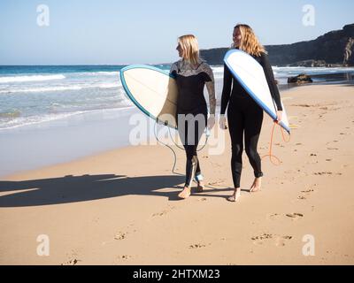 Glückliche Surferinnen, die am Strand spazieren und die Wellen beobachten Stockfoto