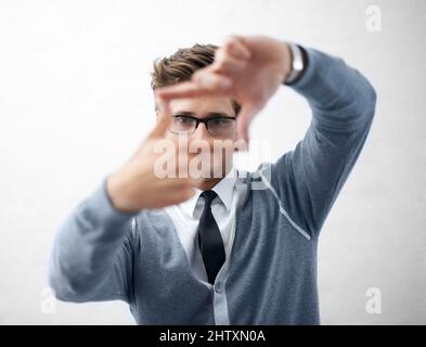 HES hat die Vision, etwas großartiges zu schaffen. Ein junger und trendiger Kerl, der eine Brille trägt und mit seinen Fingern einen Rahmen macht. Stockfoto