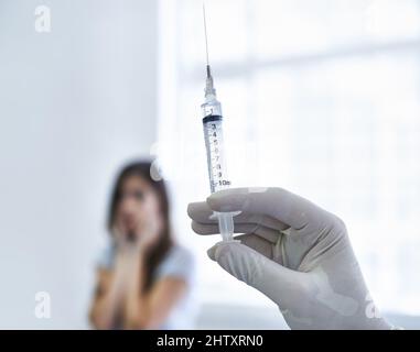 Das wird nicht ein bisschen weh tun...Ich verspreche. Ein Arzt bereitet sich darauf vor, einer nervösen jungen Frau eine Injektion zu verabreichen. Stockfoto