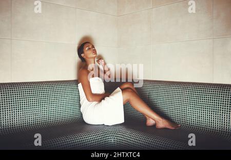 Genießen Sie die einfachen Dinge im Leben. Ganzkörperaufnahme einer jungen Frau, die sich in der Sauna in einem Spa entspannt. Stockfoto