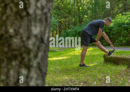 Ein junger, dauerhafter Athlet dehnt sich im Wald draußen, um den Wald, Eichen.gesunde Sportler Natur, Lifestyle-Trail Stockfoto