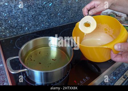 Schwäbische Küche, Zubereitung von Apfelkuchen, Einsetzen von Apfelringen in den Teig, gebackenes Fett, Dessert, Dessert, Männerhände, Kochtopf mit heißem Fett, mischen Stockfoto