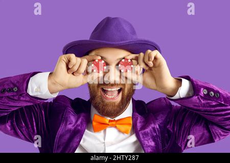 Porträt eines lustigen Mannes in violettem Anzug, der zwei Pokerchips auf den Augen hält und lächelt Stockfoto