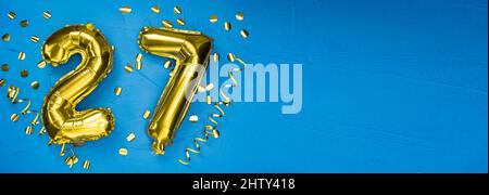 goldene Folienballon Zahl siebenundzwanzig. Geburtstags- oder Jubiläumskarte mit der Aufschrift 27. Blauer Betonhintergrund. Jubiläumsfeier. Bann Stockfoto