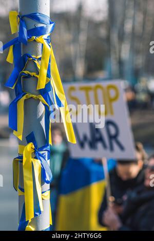 Bänder mit Farben der Ukraine während einer friedlichen Demonstration gegen den Krieg, Putin und Russland, Ukrainisch und Stop war Plakat auf Hintergrund, vertikal Stockfoto