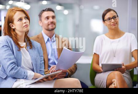 Aufmerksam auf die Präsentation achten. Aufnahme von drei Kollegen, die sich eine Präsentation anhören. Stockfoto