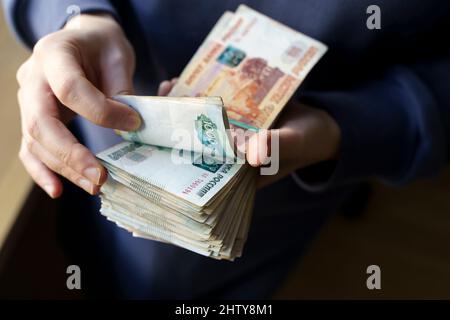 Russische Rubel Banknoten in den Händen während des Krieges in der Ukraine. Inflation, Sanktionen und der Sturz des russischen Wirtschaftskonzepts. Sinkende Bargeldeinsparungen und sinkendes Budget. Hochwertige Fotos Stockfoto