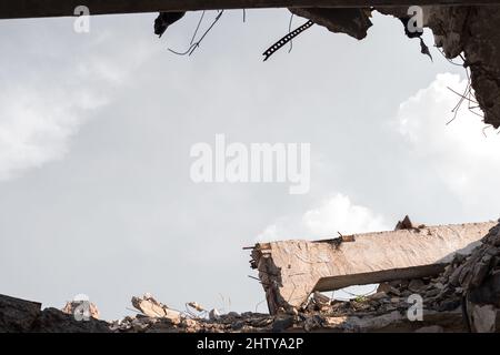 Die Ruinen der Überreste eines Gebäudes mit einem Betonbalken gegen den grauen Himmel. Ansicht von unten auf den Bruch in der Decke des Gebäudes. Hintergrund. Stockfoto