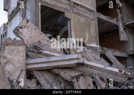 Ein großes zerstörtes Gebäude mit einem Haufen grauer Betonfragmente von Platten und Balken aus der Nähe. Hintergrund. Stockfoto