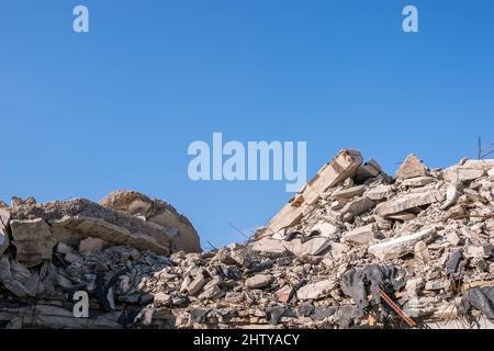 Haufen Bauabfälle in Form von Betonfragmenten aus Platten, Pfählen, Ziegel an einem sonnigen Tag gegen einen blauen, klaren Himmel. Hintergrund. Stockfoto