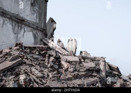 Ein zerstörtes Betongebäude mit einem Schutthaufen im Vordergrund vor grauem Himmel. Hintergrund. Stockfoto