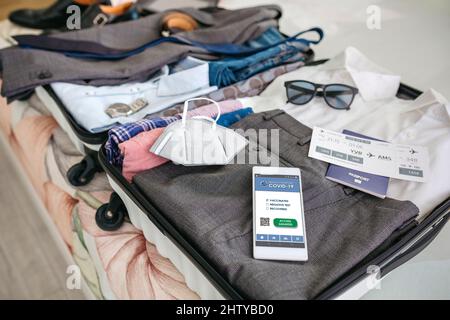 Koffer für Geschäftsreisende mit einem kovidierten Reisepass auf dem Handy Stockfoto