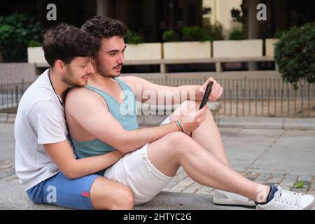 Gay paar mit dem Smartphone auf einer Bank sitzen. Stockfoto