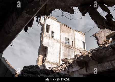 Blick durch eine Lücke in der Decke eines großen Gebäudes auf die Überreste einer Betonwand gegen den grauen Himmel. Hintergrund. Stockfoto