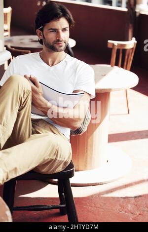 Die Welt aus der Perspektive von Künstlern betrachten. Ein hübscher junger Mann sitzt skizzenhaft in einem Café. Stockfoto