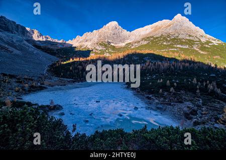 Luftaufnahme des gefrorenen Sorapiss-Sees, umgeben von bunten Lärchen und Pinien im Herbst, der Gipfel Cime del Laudo (rechts) und La Cesta (lef Stockfoto