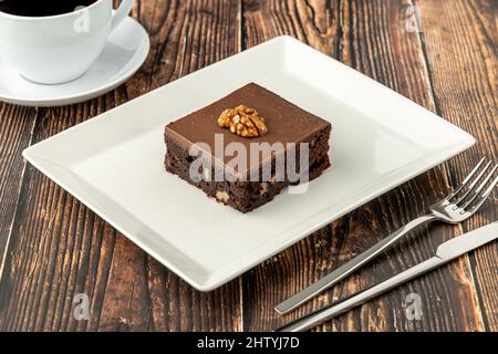 Nussbaum und dunkler Schokoladenbrownie auf einem weißen Porzellanteller auf einem Holztisch Stockfoto