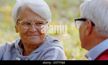 Ältere grauhaarige Großeltern lächeln einander an und reden, während sie Zeit im Freien verbringen. Hochwertige Fotos Stockfoto