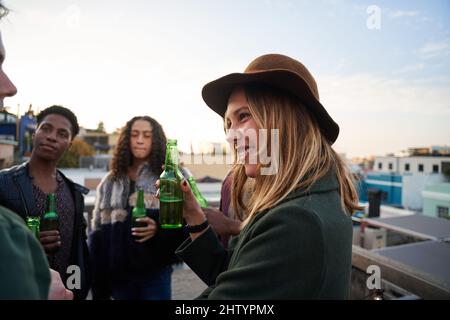 Kauskasianische Frau, die auf einer Dachparty in der Stadt mit Freunden plaudert und ihnen zuhört. Multikulturelle Gruppe von Freunden am Abend Stockfoto