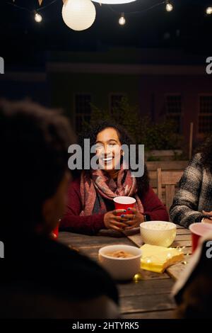Biracial junge Erwachsene weibliche Geselligkeit an einem Dachtisch. Mit Freunden am Tisch sitzen, rote Tasse halten, lachen Stockfoto