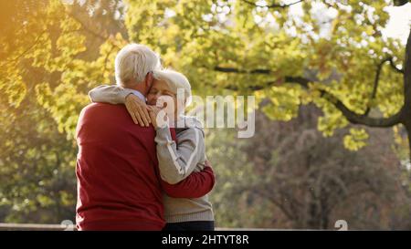 Liebevoller älterer Ehemann umarmt seine Rentnerin vor ihrem Haus. Verbringen Sie Zeit im Park und genießen Sie die frische Luft. Hochwertige Fotos Stockfoto