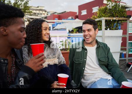 Gruppe von multikulturellen jungen erwachsenen Freunden, die über Witz zusammen lachen. Auf einer Dachparty in der Stadt zu sitzen, gute Zeiten. Stockfoto