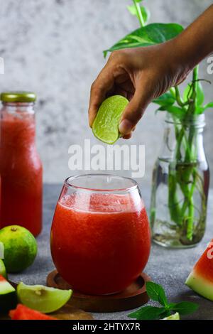Jus Semangka oder Wassermelonensaft, geschnitten auf Holzschneidebrett mit Scheiben Wassermelone und Limette. Gesundes Getränk während der Sommerferien. Stockfoto