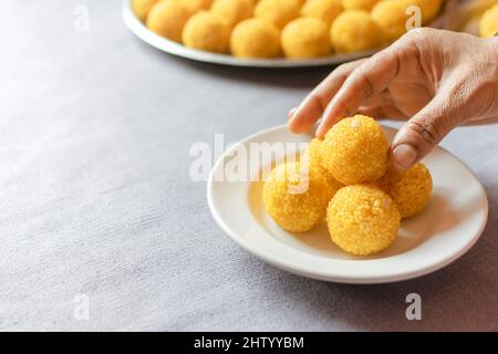 Bundi laddu mit menschlicher Hand hält es in der weißen Platte. Selektiver Fokus verwendet. Platz für Text kopieren. Laddu ist ein süßes Dessert aus Gramm Mehl. Stockfoto