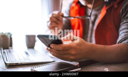 Junger hispanischer Mann mit Brille, die in seinem Büro arbeitet und sein Telefon hält Stockfoto