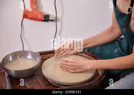 potters Hände hinter dem Töpferrad in der Töpferwerkstatt. Stockfoto