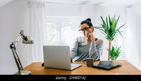 Frau mittleren Alters, die von ihrem Heimbüro aus an einem Laptop arbeitet. Weibliche Unternehmerin mit Computer für freiberufliche Arbeit. Bleiben Sie zu Hause Mama Blogger und BU Stockfoto
