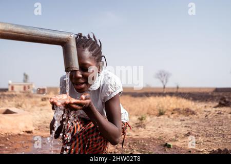 Konzept der sauberen Wasserversorgung: Junge schwarze afrikanische gebürtige Mädchen, die gesundes frisches Wasser aus einem Dorfhahn trinken Stockfoto