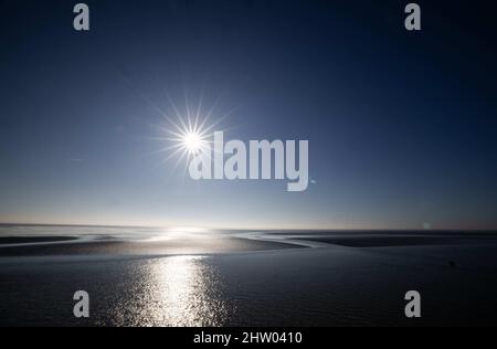 03. März 2022, Schleswig-Holstein, Dagebüll: Bei Ebbe steht die Sonne über dem Watt am Hafen von Dagebüll. Foto: Christian Charisius/dpa Stockfoto