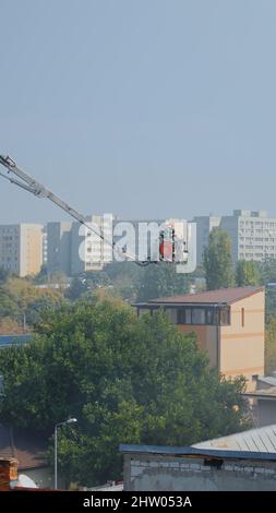 Feuerwehrleute auf dem Plattformwagen, die auf das Dach des Gebäudes fahren, um den Brand in der Stadt zu löschen. Feuerwehrleute im Haus versuchen, Flammen mit Wasser aus der Abteilung zu löschen, helfen mit Smog und Schutz Stockfoto