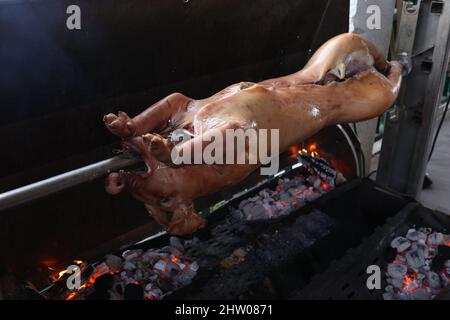 Schwein wird langsam vom Grill auf Spit in traditioneller Art, mit Holzkohle, fettes gebratenes Fleisch gekocht Stockfoto