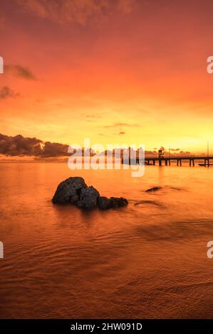 Spektakulärer, lebhafter, rot-oranger Sonnenaufgang über Palm Cove mit Austern verkrusteten Felswänden im Vordergrund, die das Interesse an dem legendären Pier in QLD, Australien, wecken. Stockfoto