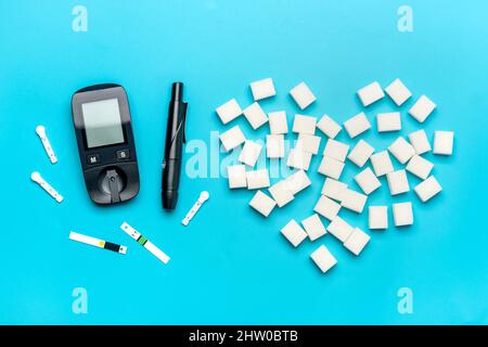 Glucometer, Zuckerwürfel auf blauem Hintergrund hohes Blutzucker- und Diabetes-Konzept Draufsicht Flat Lay 14. November - Weltdiabetestag. Stockfoto