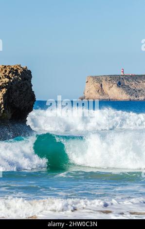 Blick auf den rot-weißen Leuchtturm von Cape St. Vincent vom wunderschönen Praia da Cordoama aus, während die Wellen einstürzen Stockfoto