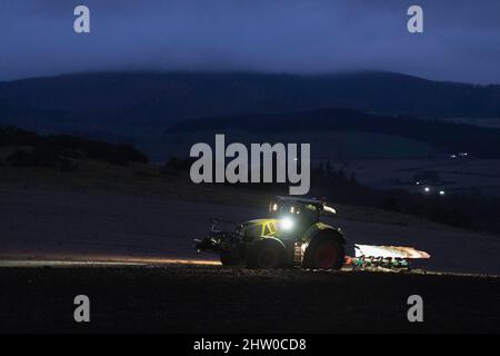 Ein Landwirt, der im Winter bis spät in den Abend auf einem Hügel in Aberdeenshire pflügt Stockfoto