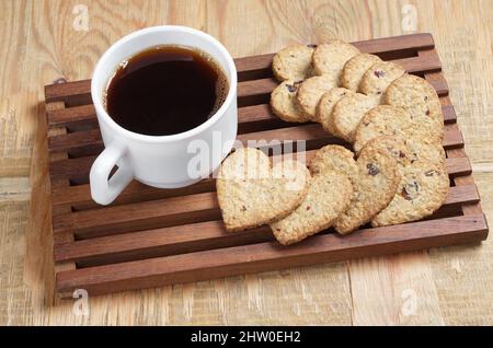 Tasse Kaffee und leckere Kekse in Herzform auf altem Holz Stockfoto