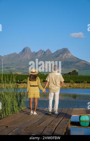Weinbergslandschaft bei Sonnenuntergang mit Bergen in Stellenbosch, nahe Kapstadt, Südafrika. Weintrauben auf Weinreben im Weinberg, Paar Mann und Frau mit Blick auf den See Stockfoto