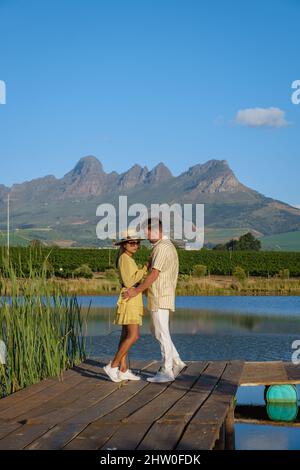 Weinbergslandschaft bei Sonnenuntergang mit Bergen in Stellenbosch, nahe Kapstadt, Südafrika. Weintrauben auf Weinreben im Weinberg, Paar Mann und Frau mit Blick auf den See Stockfoto