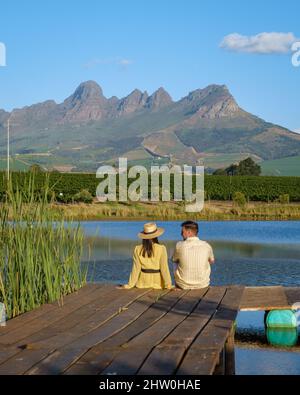 Weinbergslandschaft bei Sonnenuntergang mit Bergen in Stellenbosch, nahe Kapstadt, Südafrika. Weintrauben auf Weinreben im Weinberg, Paar Mann und Frau mit Blick auf den See Stockfoto