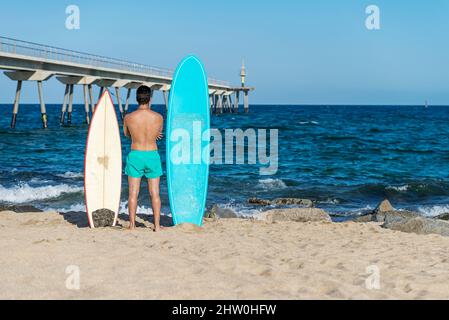 Nahaufnahme eines gutaussehenden Männerstands mit Surfbrett am Surfspot am Meeresstrand und Warten auf die Welle. Blick von hinten. Stockfoto