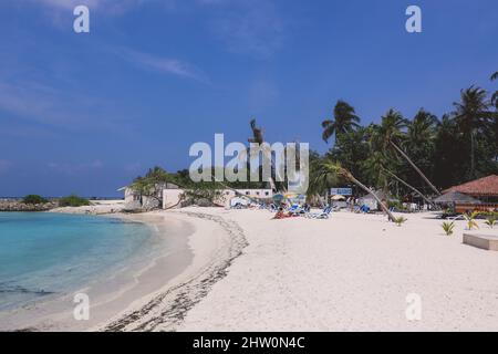 Maafushi, Malediven - 25. Juni 2021: Menschen in der Nähe des weißen Sandstrandes mit den Palmen und dem Hotelgebäude auf der maledivischen Paradies-Insel Stockfoto