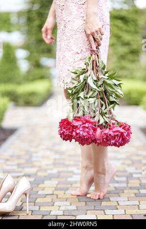 Barfuß Frau mit einem Blumenstrauß Pfingstrosen auf der Straße. Zärtlichkeit. Hochwertige Fotos Stockfoto