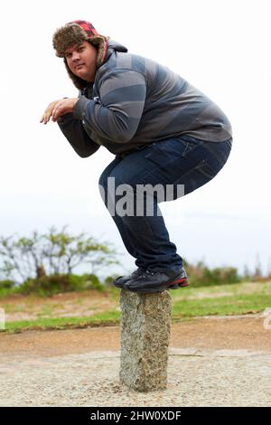 Bereit zum Stunzen. Ein übergewichtiger junger Mann im Winter trägt spielerisch auf einem Posten balanciert. Stockfoto