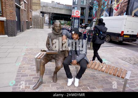 Kleiner Junge, der neben der William Shakespeare Statue in Shoreditch London, Großbritannien, sitzt Stockfoto